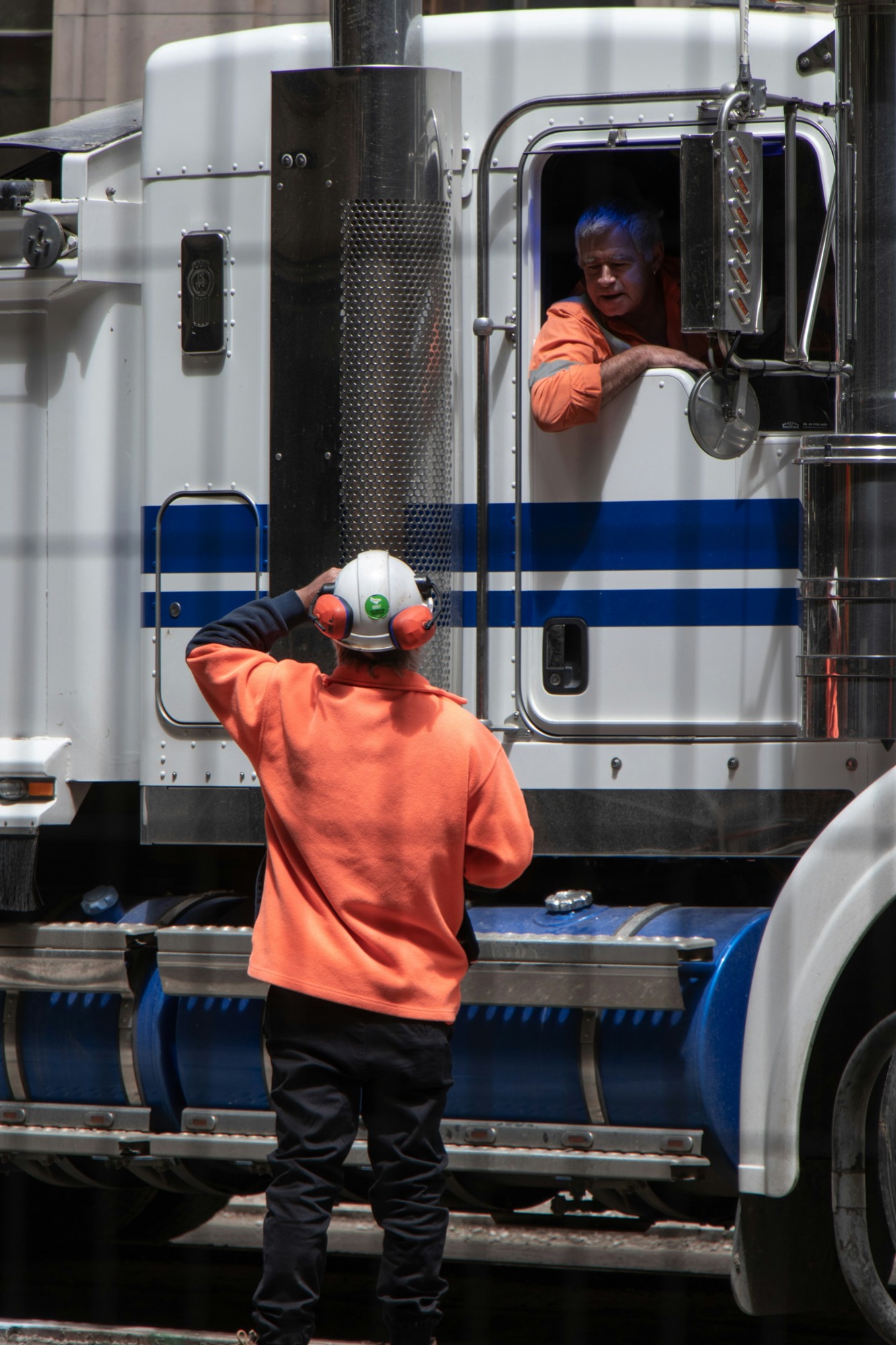 A driver leaning from the window of a tractor cab, talking to a colleague on the ground.