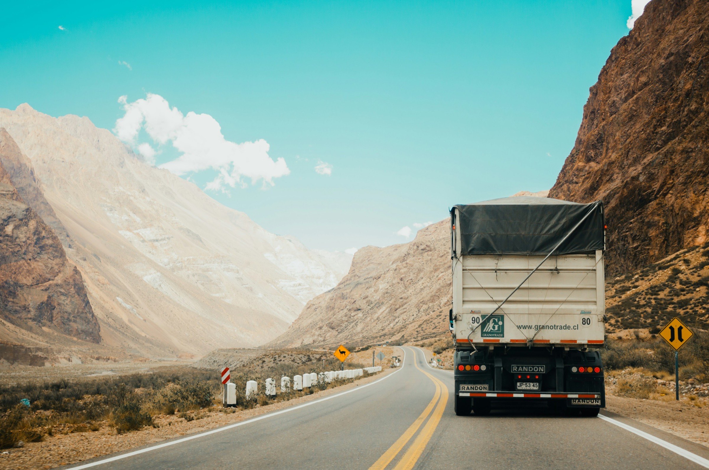 The rear of a loaded trailer on a highway running through arid mountains.