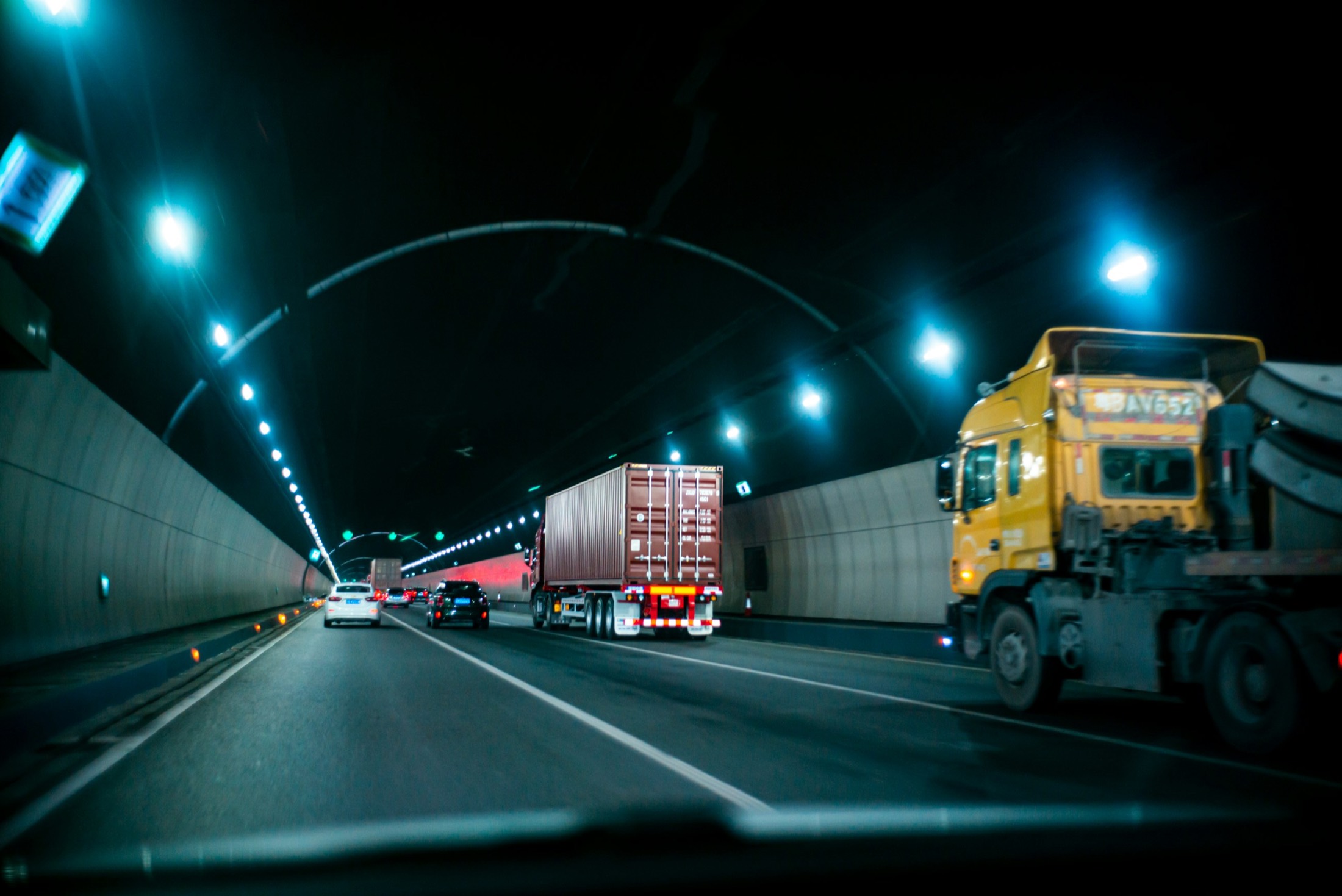 A freight truck on a lit highway at night, viewed through a windshield.